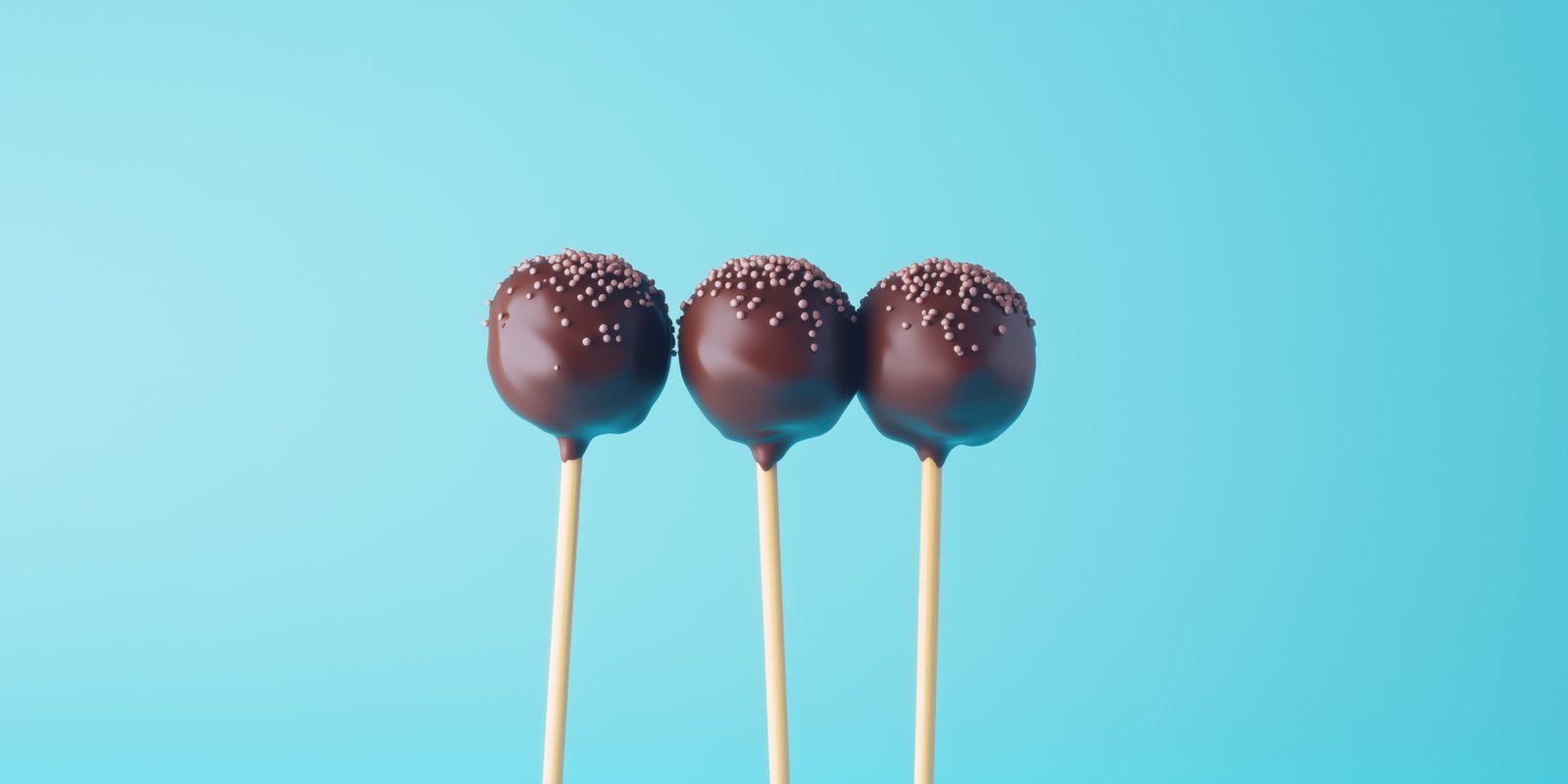 Chocolate cake pops decorated with sprinkles on sticks against a light blue background